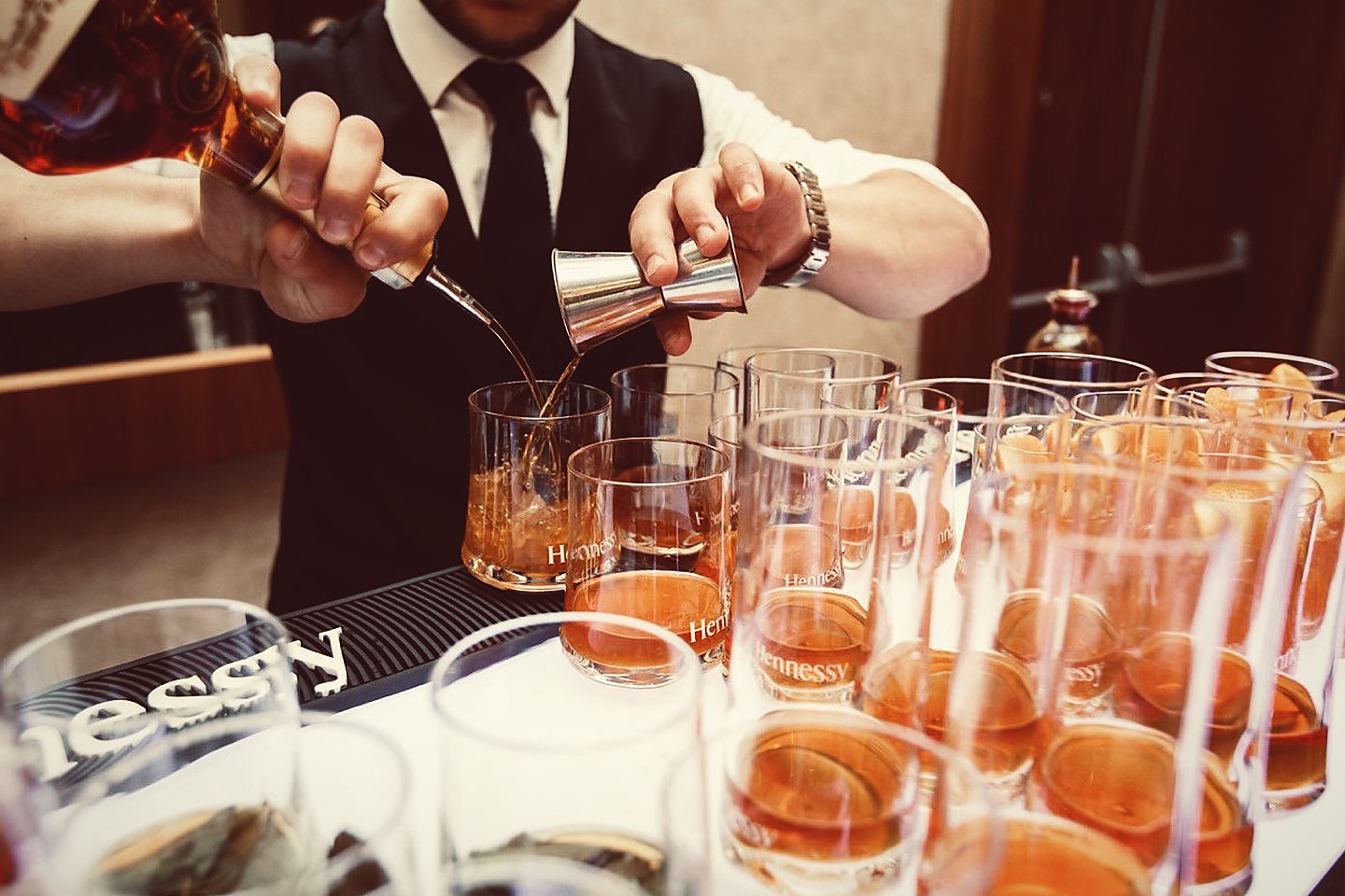 Бармен отмеряет коньяк Hennessy джиггером для коктейлей на дегустации